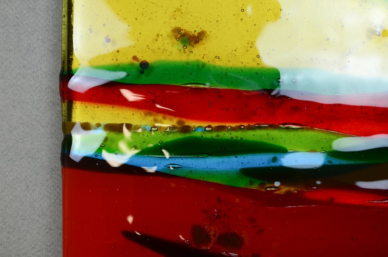 K&ouml;nnte beinhalten: Nahaufnahme eines bunten Glaskunstwerks mit Schichten aus rotem, gr&uuml;nem, blauem und gelbem Glas. Das Glas hat eine strukturierte Oberfl&auml;che und scheint handgefertigt zu sein.
