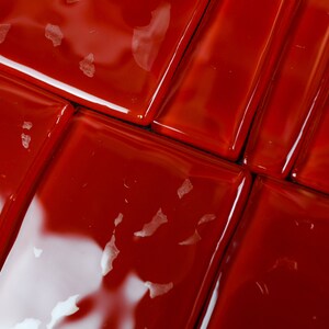 May include: Close-up of glossy, red square tiles arranged in a grid pattern. The tiles have a reflective surface, with small white flecks scattered across them. The image highlights the texture and colour of the tiles.