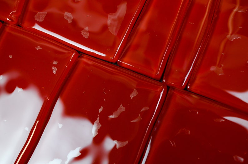 May include: Close-up of glossy, red square tiles arranged in a grid pattern. The tiles have a reflective surface, with small white flecks scattered across them. The image highlights the texture and colour of the tiles.