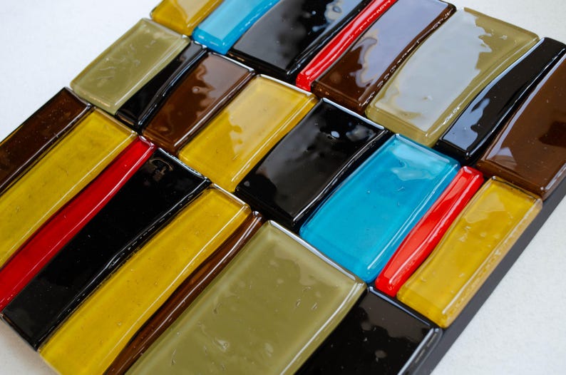 May include: A mosaic tile art piece with a geometric pattern of rectangular tiles in various colours. The tiles include shades of yellow, brown, black, red, blue, and olive green, arranged diagonally.