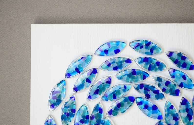 May include: A circular arrangement of blue and turquoise glass tiles, each with a unique pattern of smaller glass pieces, on a white background.