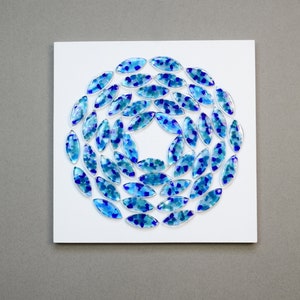 May include: A white square canvas with a circular design of blue and teal glass tiles arranged in a spiral pattern.