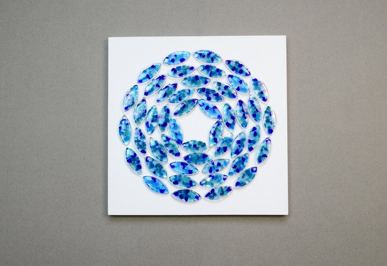 May include: A white square canvas with a circular design of blue and teal glass tiles arranged in a spiral pattern.