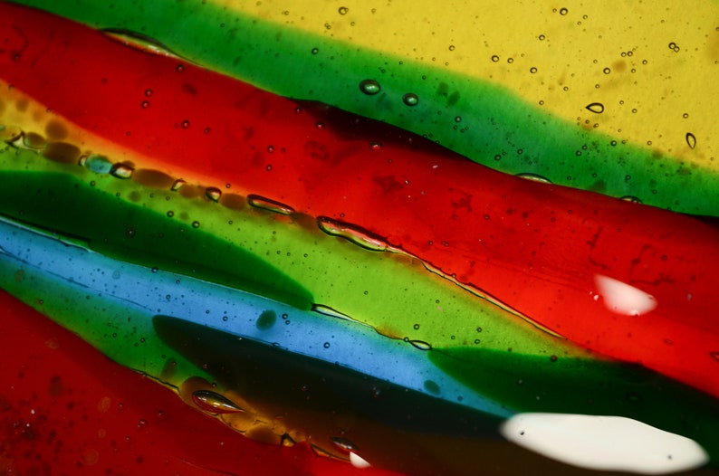 K&ouml;nnte beinhalten: Abstrakte Kunst mit einer Nahaufnahme von geschichtetem, durchsichtigem Glas mit roten, gr&uuml;nen, blauen und gelben Streifen. Das Glas hat kleine Luftblasen, die darin eingeschlossen sind.