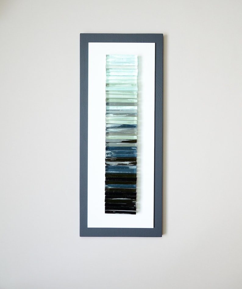 May include: A framed wall art piece featuring a vertical gradient of glass tiles in shades of blue, green, and black.