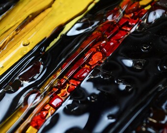 May include: Close-up of a glass art piece with layers of black, yellow, and red glass. The glass is textured and has a glossy finish.