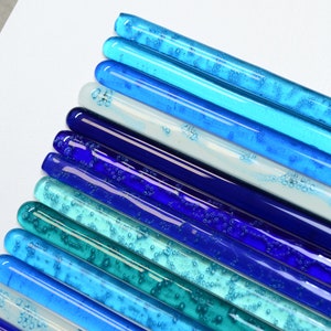 May include: A collection of glass rods in various shades of blue, from light blue to dark blue, with some rods containing air bubbles. The rods are arranged in a gradient pattern, with the lightest blue rods at the top and the darkest blue rods at the bottom.