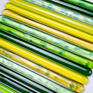 May include: A collection of glass rods in shades of green and yellow. The rods are arranged in a fan shape, with the green rods at the bottom and the yellow rods at the top.