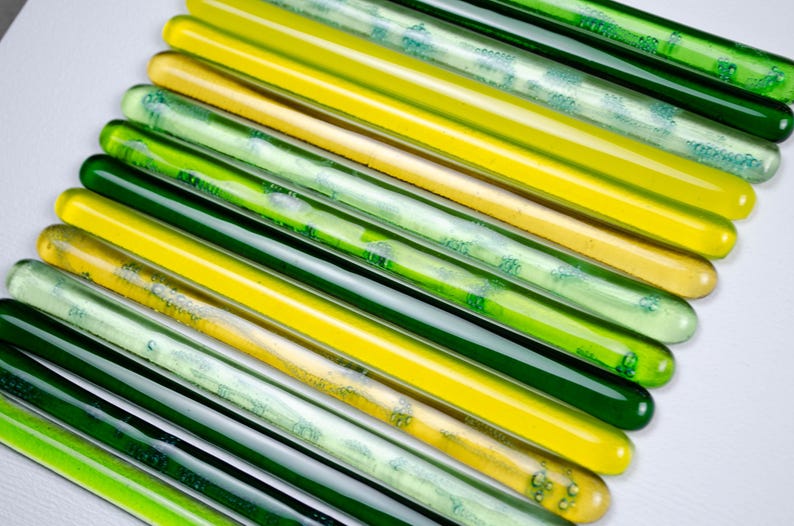 May include: A collection of glass rods in shades of green and yellow. The rods are arranged in a fan shape, with the green rods at the bottom and the yellow rods at the top.