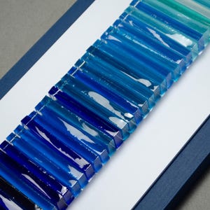 May include: A wall art piece made of glass tiles in shades of blue, arranged in a gradient pattern from dark blue to light blue.