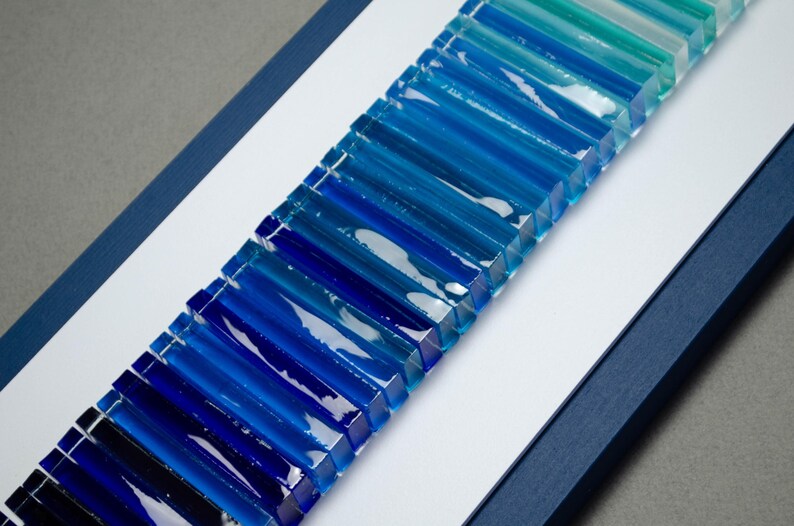 May include: A wall art piece made of glass tiles in shades of blue, arranged in a gradient pattern from dark blue to light blue.