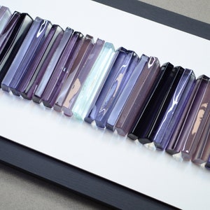 Könnte beinhalten: Ein gerahmtes Wandbild mit einer Reihe von Glasstäben in Violett-, Blau- und Weißtönen. Die Stäbe sind versetzt angeordnet und erzeugen eine optisch interessante Textur.