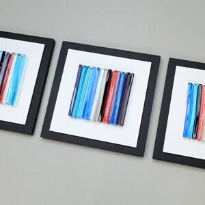 Pu&ograve; includere: Tre pezzi di arte da parete incorniciati con bacchette di vetro colorate disposte in linee verticali. Le bacchette di vetro sono in tonalit&agrave; di blu, rosso, bianco e nero.