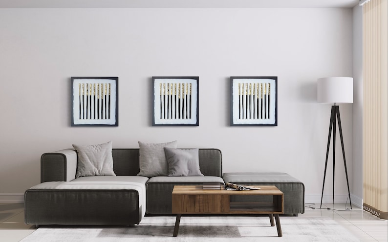 May include: Three framed black and white abstract art prints with gold accents hanging on a white wall above a gray sectional sofa and a wooden coffee table.
