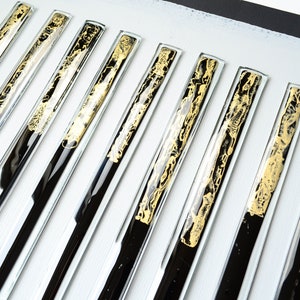 May include: A set of ten black and gold glass tiles with a decorative pattern. The tiles are arranged in a row on a white surface.