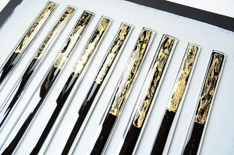May include: A set of ten black and gold glass tiles with a decorative pattern. The tiles are arranged in a row on a white surface.