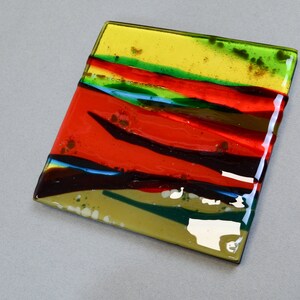 K&ouml;nnte beinhalten: Eine quadratische Glasfliese mit einem mehrschichtigen Design in Rot, Gelb, Gr&uuml;n und Braun. Das Glas ist durchscheinend und hat eine gl&auml;nzende Oberfl&auml;che.