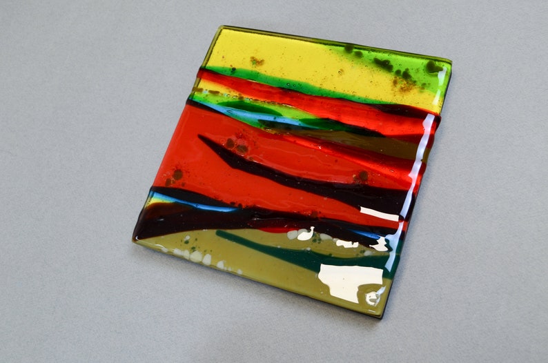 K&ouml;nnte beinhalten: Eine quadratische Glasfliese mit einem mehrschichtigen Design in Rot, Gelb, Gr&uuml;n und Braun. Das Glas ist durchscheinend und hat eine gl&auml;nzende Oberfl&auml;che.