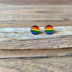 May include: A pair of rainbow-coloured wooden stud earrings. The earrings are round and have a rainbow design with red, orange, yellow, green, blue, indigo, and violet stripes.