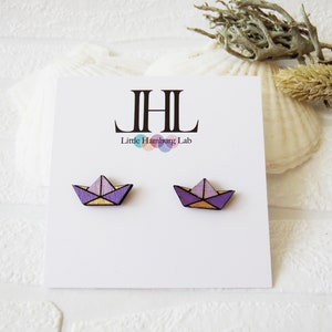 Könnte beinhalten: Ein Paar Holzohrringe in Form von Origami-Papierbooten. Die Boote sind in Violett-, Rosa- und Gelbtönen bemalt. Die Ohrringe befinden sich auf einer weißen Karte mit dem Text "JHL Little Hamburg Lab".
