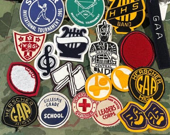 May include: A collection of various embroidered fabric patches featuring diverse shapes and designs, including sports logos, musical instruments, school emblems, and text such as Steger Invitational Tournament, HHS Band, GAA, WHS, and Herscher Gap High.
