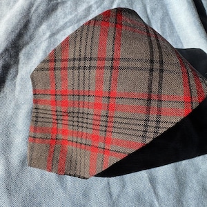 May include: A plaid face mask in shades of brown, red, and black. The mask features a classic plaid pattern with intersecting lines. The fabric appears to be a woven material, and the mask is folded.