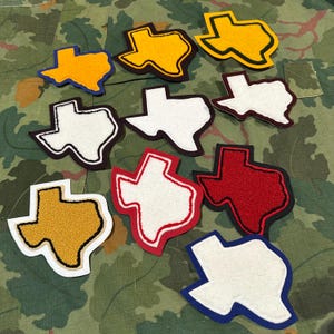 Peut inclure: Collection d'écussons brodés en forme de l'État du Texas. Les écussons présentent diverses combinaisons de couleurs, notamment le jaune, le blanc, le rouge et le bleu, avec des bordures contrastées. Idéal pour les vêtements ou les accessoires.