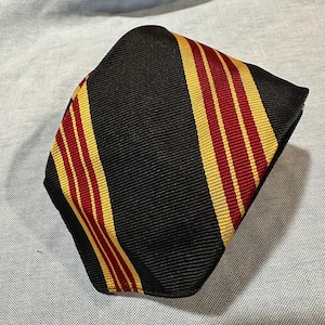 May include: A black necktie with alternating stripes of gold and burgundy. The tie is made of a textured fabric and is folded over. The tie is a classic accessory for formal or business attire.