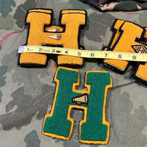 May include: Three letter H patches with textured chenille surfaces. Two are yellow with black borders and one is green with yellow borders. A yellow measuring tape shows the width of the top left patch is approximately 4 inches wide.