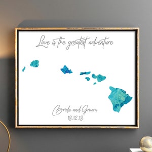 May include: A watercolor painting of the Hawaiian islands with the text "Love is the greatest adventure" and "Bride and Groom 12.12.18" in a gold frame.