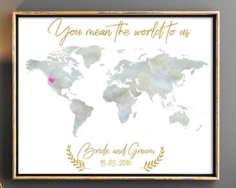 May include: A watercolor world map print with a pink heart marking a location. The print is framed in gold and has the text "You mean the world to us" and "Bride and Groom 15.05.2016" in gold lettering.