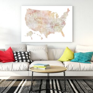 K&ouml;nnte beinhalten: Ein wei&szlig;es Sofa mit bunten Kissen in einem Wohnzimmer. Ein Aquarellbild der Karte der Vereinigten Staaten h&auml;ngt an der Wand &uuml;ber dem Sofa. Ein schwarz-wei&szlig; gemusterter Teppich liegt auf dem Boden vor dem Sofa.