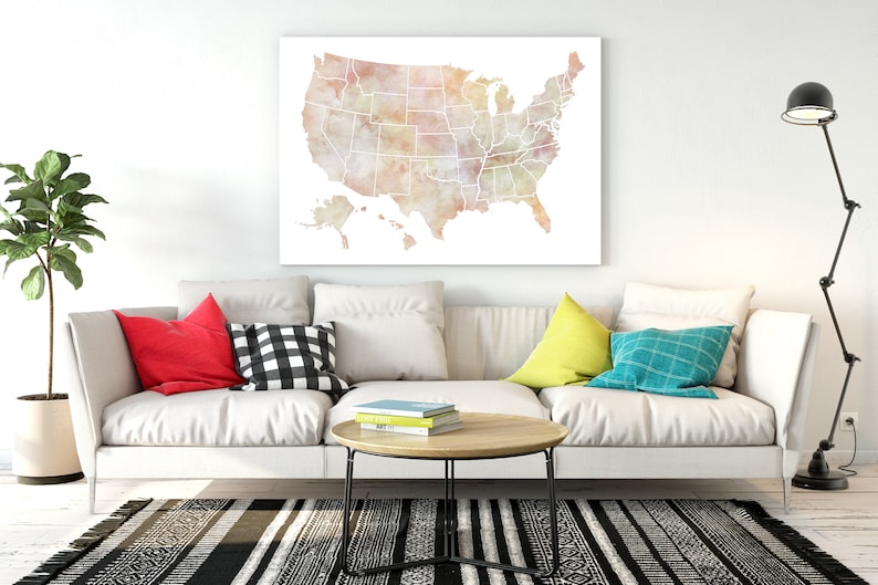 K&ouml;nnte beinhalten: Ein wei&szlig;es Sofa mit bunten Kissen in einem Wohnzimmer. Ein Aquarellbild der Karte der Vereinigten Staaten h&auml;ngt an der Wand &uuml;ber dem Sofa. Ein schwarz-wei&szlig; gemusterter Teppich liegt auf dem Boden vor dem Sofa.