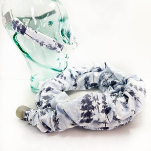 Pu&ograve; includere: Un set di copritubo per macchina CPAP e copricinghia per testiera in tessuto bianco con stampa di foresta di pini blu scuro. Le coperture in tessuto sono progettate per adattarsi al tubo medico e alle cinghie, mostrate su una testa di manichino.
