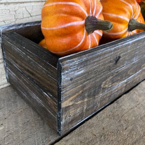 May include: A rustic wooden box with a distressed white finish, filled with orange pumpkins with white stripes. The box is made of reclaimed wood and has a natural, weathered look.