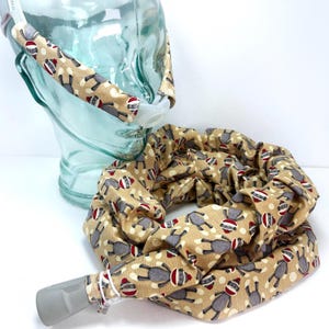 May include: A tan fabric neck gaiter and headband set. The fabric features a repeating pattern of gray sock monkeys wearing red and white striped hats. The headband is attached to a clear plastic head form.