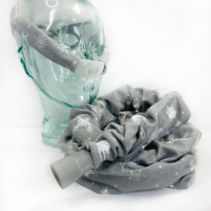 May include: A gray fabric CPAP hose cover with a white snowflake pattern. The cover is coiled and has a gray silicone connector at one end.