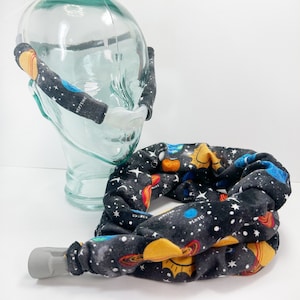 May include: A black fabric tube with a space-themed pattern featuring planets, stars, and the sun. The tube is connected to a clear plastic device. The planets are labeled with their names. The tube is designed to cover the device.