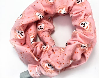 May include: Pink fabric hair scrunchie with a white skull and crossbones pattern. The scrunchie is made of a soft, stretchy fabric and has a white elastic band.