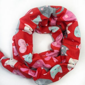 May include: Red fabric scarf with a repeating pattern of cartoon cats and hearts. The scarf is rolled into a circle.