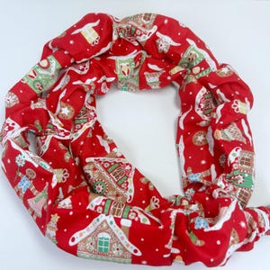 May include: A red fabric wreath with a repeating pattern of gingerbread houses, gingerbread people, and other holiday-themed designs. The wreath is circular and appears to be made of a soft, padded material.