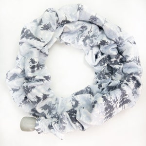 Pu&ograve; includere: Una sciarpa ad anello color azzurro con un motivo di alberi di bosco grigio scuro. Il tessuto &egrave; arricciato e disposto in forma circolare, con una piccola chiusura a levetta in plastica grigia visibile sul bordo inferiore sinistro.