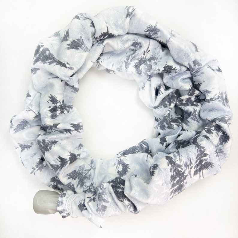 Pu&ograve; includere: Una sciarpa ad anello color azzurro con un motivo di alberi di bosco grigio scuro. Il tessuto &egrave; arricciato e disposto in forma circolare, con una piccola chiusura a levetta in plastica grigia visibile sul bordo inferiore sinistro.