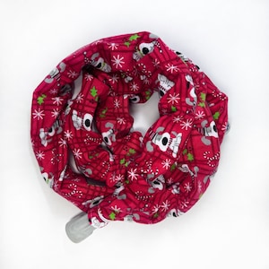 May include: A red Christmas-themed scrunchie with a pattern of white polar bears, snowflakes, and candy canes. The fabric is folded and gathered, with a gray plastic clasp visible at the end. The scrunchie is designed for hair accessories.