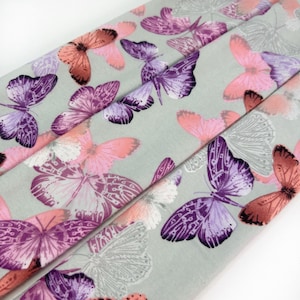 May include: A gray fabric with a repeating pattern of pink and purple butterflies. The butterflies are in various sizes and positions.