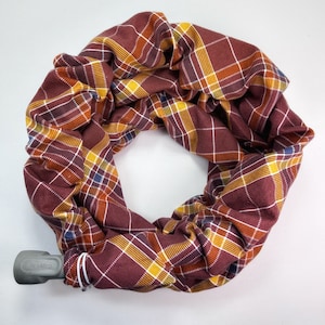 May include: A brown and yellow plaid fabric tube with a gray medical device attached. The fabric is gathered and bunched up, creating a circular shape.