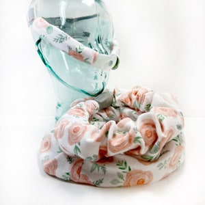 May include: A white fabric headband with a floral pattern featuring pink roses and green leaves. The headband is designed to fit around a CPAP mask.