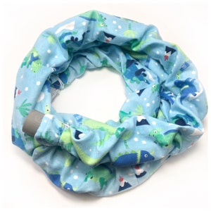 May include: A light blue infinity scarf with a white background and a repeating pattern of green and blue dinosaurs.