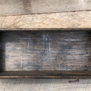 May include: A dark wood rectangular box with a distressed finish. The box has a raised lip around the edge and is empty.