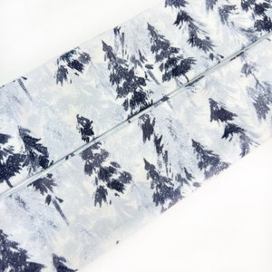Pu&ograve; includere: Una striscia di tessuto con un motivo ripetuto di alberi sempreverdi blu navy scuro su uno sfondo bianco e grigio chiaro. Il tessuto presenta una trama visibile ed &egrave; piegato diagonalmente attraverso l'inquadratura.